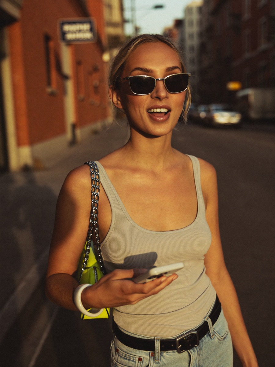 UGC-style fashion portrait of a woman in mirrored sunglasses at golden hour on a city street
